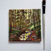 hand holding canvas of wooded trees with light shining through onto creek